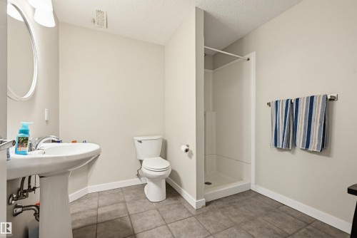 Bathroom featuring a white pedestal sink, toilet, and stand-up shower with a white surround - 11 3380 28A Avenue Nw, Edmonton, AB - Indoor Photo Showing Laundry Room