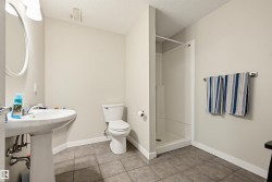Bathroom featuring a white pedestal sink, toilet, and stand-up shower with a white surround - 