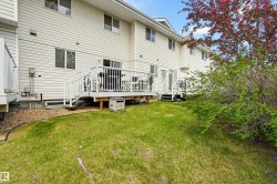 Rear exterior featuring two elevated wooden decks with white railings and stairs, white vinyl siding, multiple windows, and a grassy backyard with mature landscaping - 