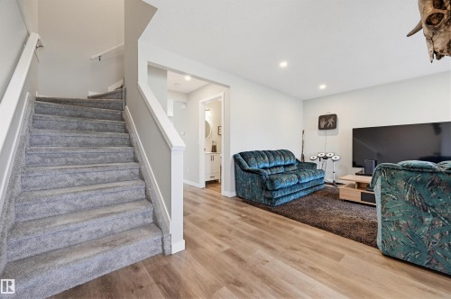 Carpeted staircase with white railings, wood-finish flooring, recessed lighting, and a partial bathroom with a white vanity and round mirror - 11 3380 28A Avenue Nw, Edmonton, AB - Indoor Photo Showing Living Room
