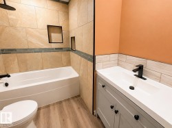 Bathroom featuring a full tub and shower with tile surround, built-in shower niches, a wood-finish floor, a white vanity with integrated sink, and a black faucet - 