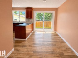 Open-concept area featuring wood-finish flooring, a kitchen island with dark cabinetry, a subway tile backsplash, and a sliding glass door leading to an outdoor deck - 