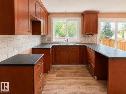 U-shaped kitchen featuring wood cabinetry, dark countertops, a tile backsplash, wood-finish flooring, and a stainless steel sink - 