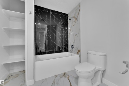 Bathroom featuring a white soaking tub with dark marbled tile surround, white marbled tile flooring, and integrated shelving - 5118 17A Avenue Nw, Edmonton, AB - Indoor Photo Showing Bathroom