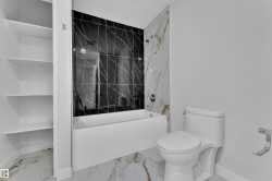 Bathroom featuring a white soaking tub with dark marbled tile surround, white marbled tile flooring, and integrated shelving - 