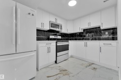 Bright kitchen featuring white cabinetry, black marble-look backsplash, stainless steel appliances, and large format floor tiling - 