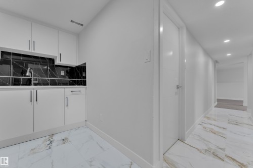 Modern kitchenette featuring white cabinetry, a stainless steel sink, and a black marble-patterned backsplash - 5118 17A Avenue Nw, Edmonton, AB - Indoor