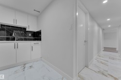 Modern kitchenette featuring white cabinetry, a stainless steel sink, and a black marble-patterned backsplash - 