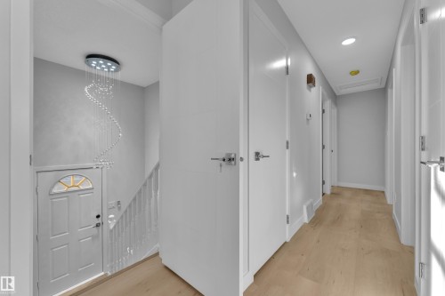 Entryway featuring a modern spiral chandelier, light wood-finish flooring, white paneled doors, and a staircase with white railings - 5118 17A Avenue Nw, Edmonton, AB - Indoor Photo Showing Other Room