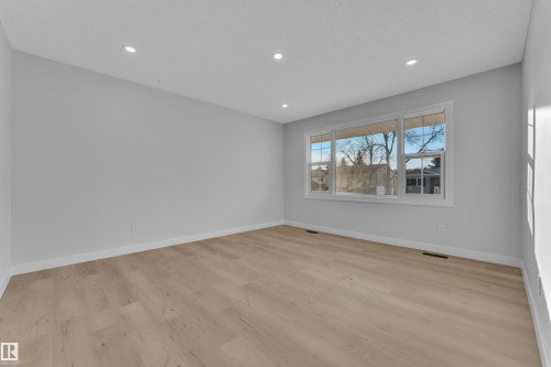Spacious room featuring wood-finish flooring, recessed ceiling lighting, a large triple window, and white baseboards - 5118 17A Avenue Nw, Edmonton, AB - Indoor Photo Showing Other Room