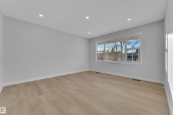 Spacious room featuring wood-finish flooring, recessed ceiling lighting, a large triple window, and white baseboards - 