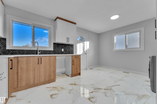 Kitchen featuring white upper cabinetry with wood trim, wood-finish lower cabinetry, and black hexagonal tile backsplash - 5118 17A Avenue Nw, Edmonton, AB - Indoor Photo Showing Kitchen