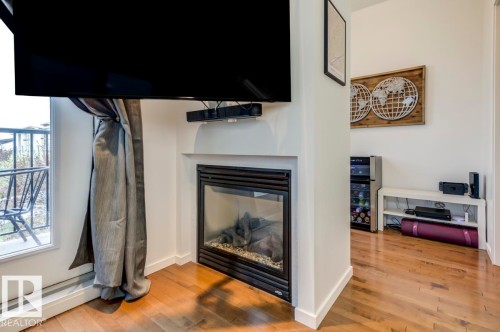 Built-in fireplace with a black surround set into a white mantel, complemented by wood-finish flooring and a white baseboard trim - 67 603 Watt Boulevard, Edmonton, AB - Indoor With Fireplace
