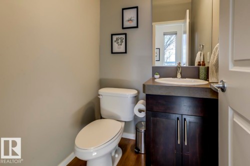 Compact powder room featuring a white toilet, wood-finish flooring, and a dark wood vanity with an integrated sink and countertop - 67 603 Watt Boulevard, Edmonton, AB - Indoor Photo Showing Bathroom