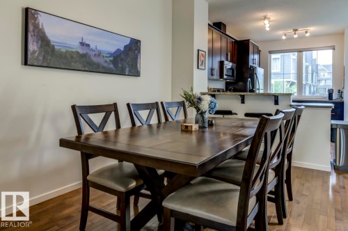 Open-concept dining area featuring wood-finish flooring, a kitchen pass-through with a countertop, dark wood cabinetry, and a large window - 67 603 Watt Boulevard, Edmonton, AB - Indoor Photo Showing Dining Room
