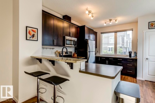 Kitchen featuring dark wood-finish cabinetry, stainless steel appliances, and a breakfast bar with stone-finish countertops - 67 603 Watt Boulevard, Edmonton, AB - Indoor Photo Showing Kitchen