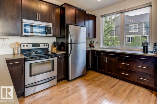 Kitchen featuring dark wood cabinetry, stainless steel appliances, light countertops, and wood-finish flooring - 67 603 Watt Boulevard, Edmonton, AB - Indoor Photo Showing Kitchen