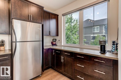 Kitchen featuring dark wood cabinetry, stainless steel refrigerator, light countertops, and a large window - 67 603 Watt Boulevard, Edmonton, AB - Indoor Photo Showing Kitchen