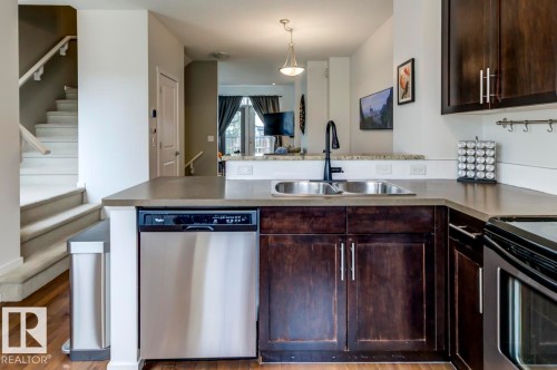 Kitchen featuring dark wood cabinetry, a stainless steel double basin sink with a matte black faucet, and a stainless steel dishwasher - 67 603 Watt Boulevard, Edmonton, AB - Indoor Photo Showing Kitchen With Double Sink