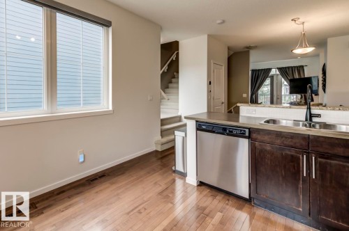 Kitchen featuring dark wood cabinetry, stainless steel dishwasher, an undermount sink with a matte black faucet, and a light-colored countertop - 67 603 Watt Boulevard, Edmonton, AB - Indoor Photo Showing Kitchen With Double Sink