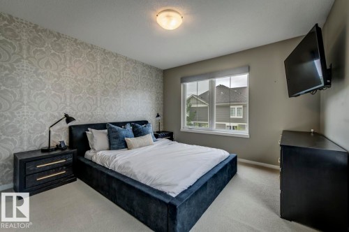 Interior room featuring a patterned accent wall, neutral wall paint, and a double-pane window with a roller shade - 67 603 Watt Boulevard, Edmonton, AB - Indoor Photo Showing Bedroom