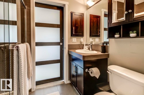 Contemporary bathroom featuring a dark wood vanity with an integrated sink, a large wall mirror, and a sleek glass-enclosed shower - 67 603 Watt Boulevard, Edmonton, AB - Indoor Photo Showing Bathroom