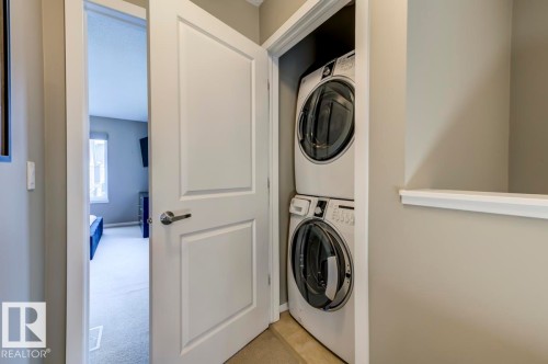 Dedicated laundry closet featuring a stacked washer and dryer unit, neutral wall paint, and white trim - 67 603 Watt Boulevard, Edmonton, AB - Indoor Photo Showing Laundry Room