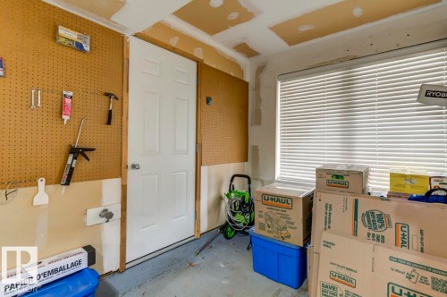 Garage space featuring a paneled door, pegboard wall, and a window with horizontal blinds - 67 603 Watt Boulevard, Edmonton, AB - Indoor