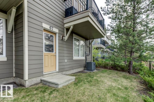 Exterior featuring horizontal siding, a concrete stoop, a light-colored entry door with window, and an overhead balcony with black metal railing - 67 603 Watt Boulevard, Edmonton, AB - Outdoor