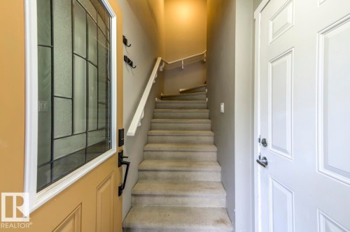 Entryway featuring a decorative glass panel door with a dark bronze handle, a carpeted staircase with a white handrail, and a paneled interior door with chrome hardware - 67 603 Watt Boulevard, Edmonton, AB - Indoor Photo Showing Other Room
