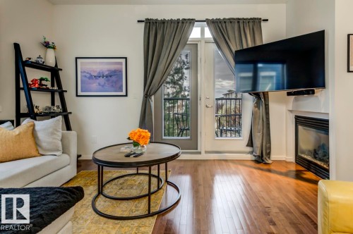 Living area featuring wood-finish flooring, a built-in fireplace, and a glass-paned door leading to an outdoor balcony with a metal railing - 67 603 Watt Boulevard, Edmonton, AB - Indoor Photo Showing Living Room With Fireplace