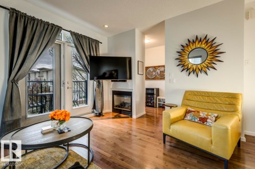 Living area featuring wood-finish flooring, a built-in fireplace, and double glass doors leading to an outdoor balcony - 67 603 Watt Boulevard, Edmonton, AB - Indoor Photo Showing Living Room With Fireplace