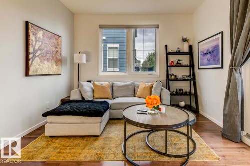 Living area featuring wood-finish flooring, white baseboards, and a window with a roller shade - 67 603 Watt Boulevard, Edmonton, AB - Indoor Photo Showing Living Room