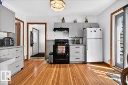 Kitchen featuring light wood-finish flooring, light grey cabinetry with black hardware, black cooking range with overhead exhaust, and a white refrigerator - 
