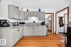Kitchen featuring light gray shaker-style cabinetry, a light-toned countertop, a tile backsplash, wood-finish flooring, and a stainless steel sink with a pull-down faucet - 