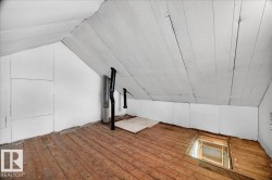 Attic space featuring wood-finish flooring, white paneled walls, and a sloped ceiling - 