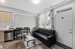 Compact living area featuring wood-finish flooring, a kitchen counter with stainless steel appliances, and light-toned cabinetry - 