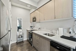 Modern kitchen featuring stainless steel appliances, light-toned cabinetry, white countertops, a stainless steel sink, and wood-finish flooring - 