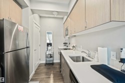 Galley kitchen featuring stainless steel appliances, light wood-finish upper cabinetry, and a white countertop - 