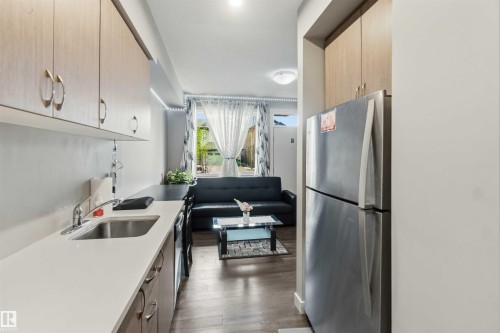 Compact kitchen area featuring wood-finish cabinetry, a stainless steel sink, and light-toned countertops - 456 Allard Boulevard, Edmonton, AB - Indoor Photo Showing Kitchen