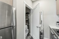 Integrated laundry closet with white stackable appliances, adjacent to a stainless steel refrigerator - 