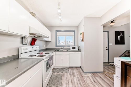 Kitchen featuring white cabinetry and appliances, grey countertops, wood-finish flooring, and a window with blue trim - 214A Warwick Road, Edmonton, AB - Indoor Photo Showing Kitchen With Double Sink