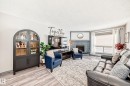 Living area featuring wood-finish flooring, a brick fireplace with a white mantel, and a large window with blinds - 214A Warwick Road, Edmonton, AB  - Indoor Photo Showing Living Room With Fireplace 