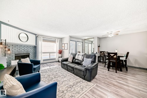 Spacious living area featuring a painted brick fireplace with a shiplap accent wall, wood-finish flooring, and large windows - 214A Warwick Road, Edmonton, AB - Indoor Photo Showing Living Room With Fireplace