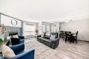 Spacious living area featuring a painted brick fireplace with a shiplap accent wall, wood-finish flooring, and large windows - 214A Warwick Road, Edmonton, AB  - Indoor Photo Showing Living Room With Fireplace 