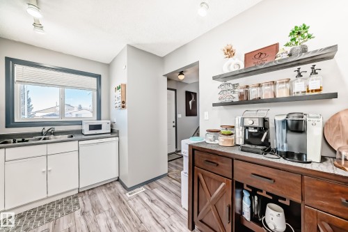 Kitchen area featuring wood-finish flooring, white cabinetry, a built-in dishwasher, and a window with blinds - 214A Warwick Road, Edmonton, AB - Indoor Photo Showing Kitchen With Double Sink