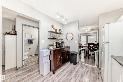 Interior space featuring wood-finish flooring, a built-in dark wood-tone cabinet, and an open doorway revealing a dining area with a ceiling fan and a window with an arched transom - 214A Warwick Road, Edmonton, AB - Indoor Photo Showing Other Room