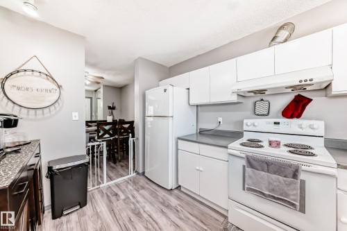 Well-appointed kitchen featuring wood-finish flooring, white cabinetry, a white electric range, and a white refrigerator - 214A Warwick Road, Edmonton, AB - Indoor Photo Showing Kitchen