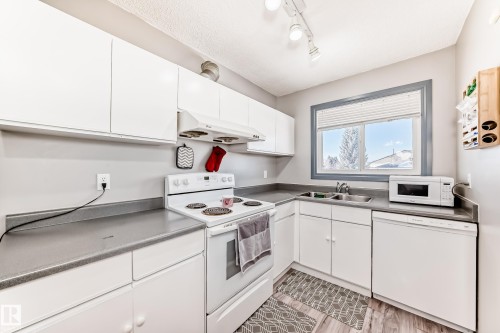Kitchen featuring white cabinetry, grey countertops, white appliances, and wood-finish flooring - 214A Warwick Road, Edmonton, AB - Indoor Photo Showing Kitchen With Double Sink