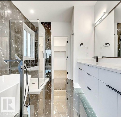 Modern bathroom featuring dark marbled tile flooring and shower surround, a freestanding tub with a matte black floor-mounted faucet, a glass-enclosed shower, and a double vanity with a light-colored countertop - 13032 186 Avenue, Edmonton, AB - Indoor Photo Showing Bathroom